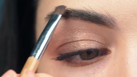 eyebrow makeup close-up. eye of a young model during makeup, makeup artist paints with a brush the eyebrow of a brunette girl. the use of cosmetics, macro shot