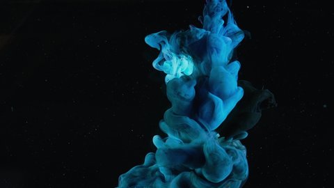Blue paint drops mixing in water slow motion. Stock footage. Smooth ink swirling and splashing from above underwater leaving ink cloud on black background.