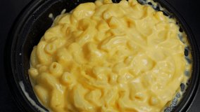 This POV closeup video shows a plastic spoon stirring and serving bowl of delicious macaroni and cheese.