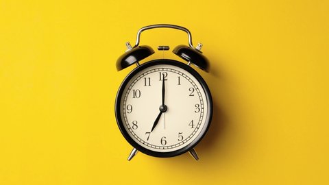 Time on vintage black alarm clock running from 7.00 to 8.00 isolated on yellow background color. One hour time lapse of black alarm clock running from 7.00 to 8.00.