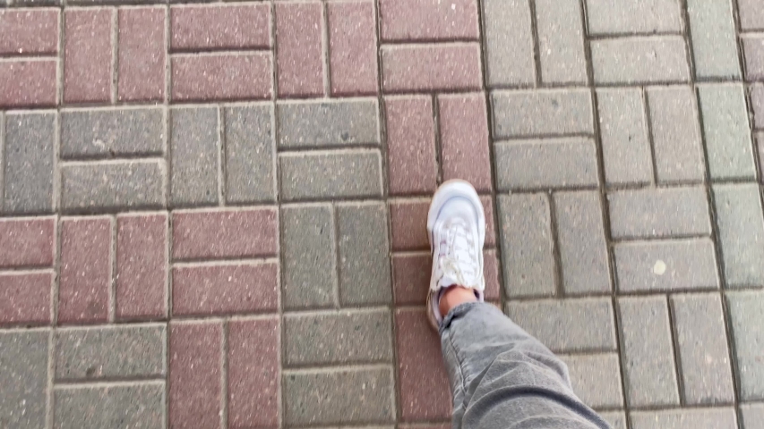 Female legs in wide gray jeans and white sneakers walk on a stone tile, on which hatches are periodically visible. | Shutterstock HD Video #1052817776