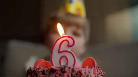 Close up of kid blowing out candle with number 6 on chocolate birthday cake in slow motion. Six years old boy celebrates birthday. 