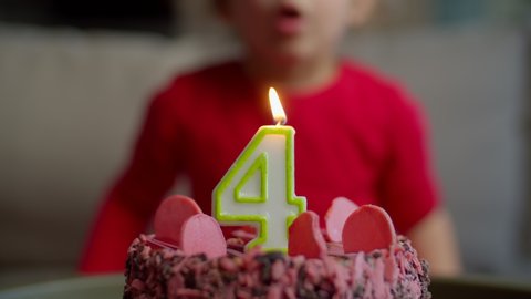 Close up of kid blowing out candle with number 4 on chocolate birthday cake in slow motion. Four years old girl celebrates birthday. 