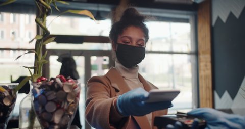 Customer black woman paying for coffee using NFC technology with phone and credit card, contactless payment with student girl woman after coronavirus quarantine pandemic.
