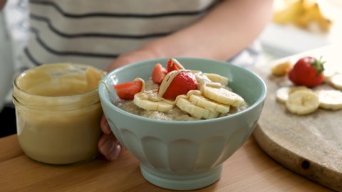 Oatmeal porridge with banana, strawberry and nut butter. Adding nut butter to breakfast porridge, healthy vegan breakfast