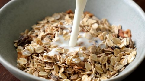 Slow motion milk pouring in bowl of muesli breakfast cereals. Healthy food
