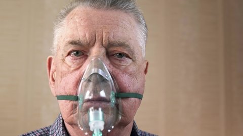 Portrait of an elderly man with COPD in an oxygen mask who is breathing deeply. Theme of a serious and incurable disease of lungs and respiratory system. Grandfather breathes in a special medical mask