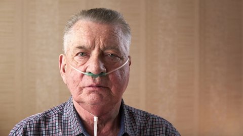 Portrait of an old man with a medical nasal oxygen catheter deep breathing. Theme of a serious and incurable disease of lungs and respiratory system. Grandfather breathes in a special medical mask