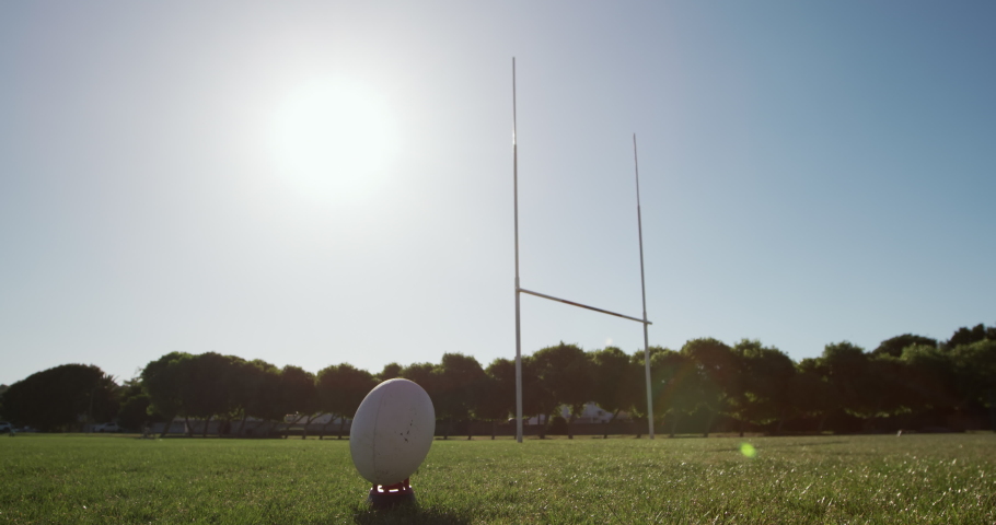 Rear view low section of a teenage mixed-race male rugby player wearing a red and white team strip, kicking a rugby ball on a playing field in slow motion Royalty-Free Stock Footage #1052828861