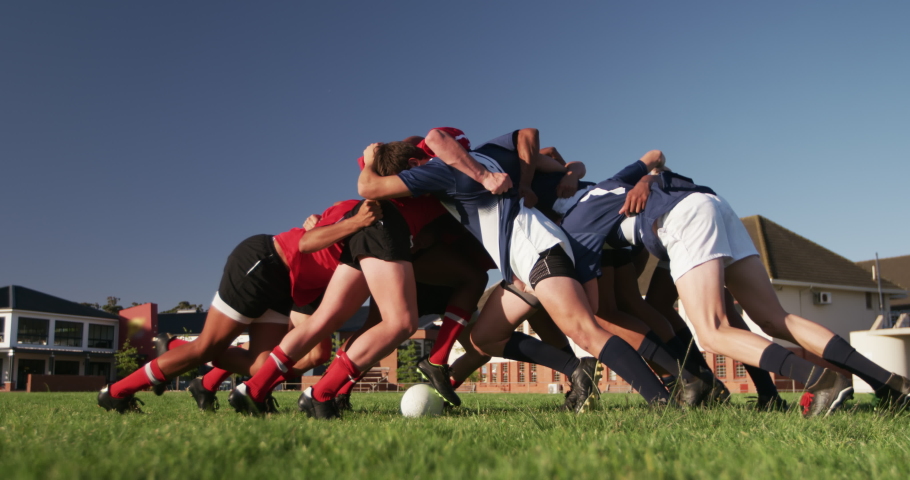 Side view of two teenage multi-ethnic male teams of rugby players wearing their team strips, in action, forming a scrum, during a rugby match on a playing field in slow motion Royalty-Free Stock Footage #1052829389