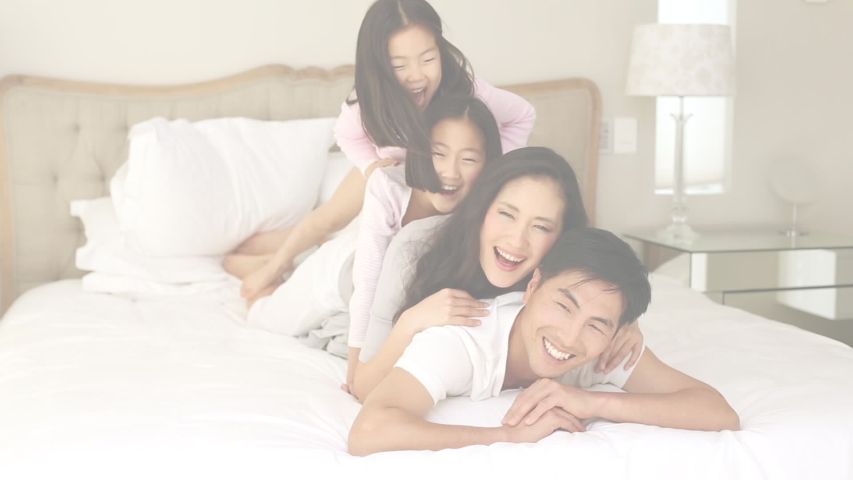 Animation of U.S. flag over Asian family playing on bed. United States of America presidential election democracy holiday concept digital composition