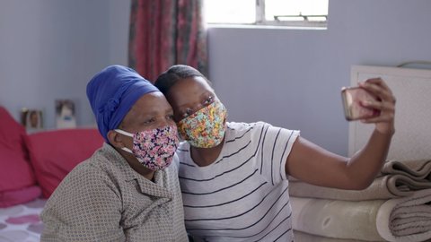 Black South African mother and daughter take selfies in their home wearing their covid-19 coronavirus protective masks. 