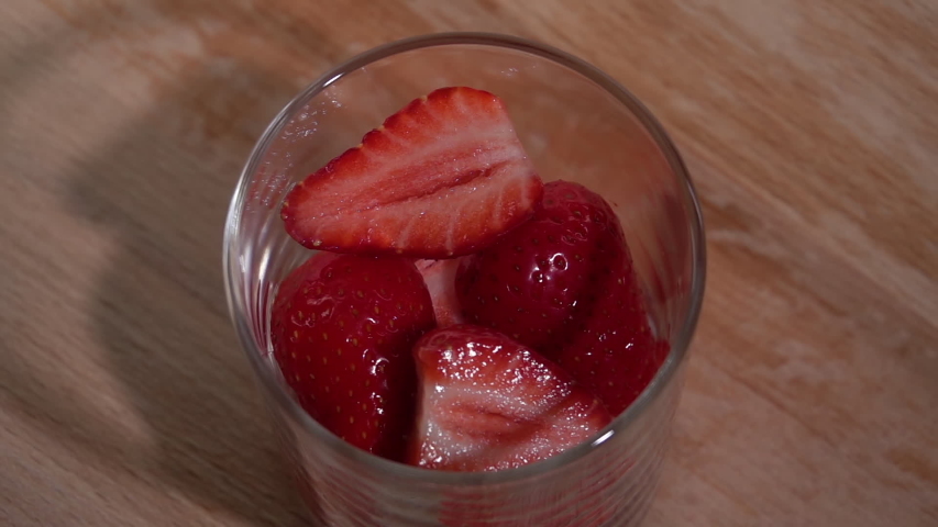 Pour milk onto a strawberry in a glass cup. Slow motion 250fps