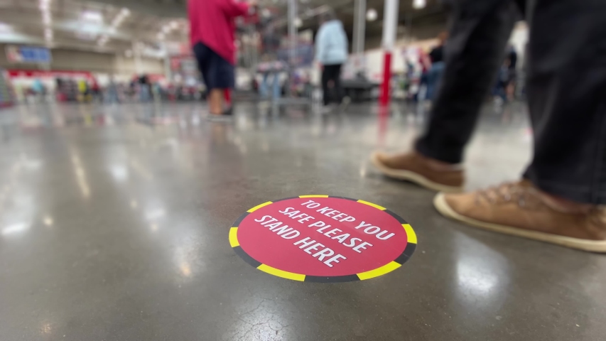 A low angle view of a social distance reminder sticker on the floor of a large big box warehouse store.	 Royalty-Free Stock Footage #1052832113