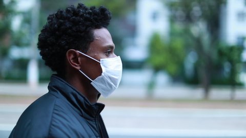 Black man walking city sidewalk wearing surgical mask for outbreak prevention, african person walking in urban environment วิดีโอสต็อก