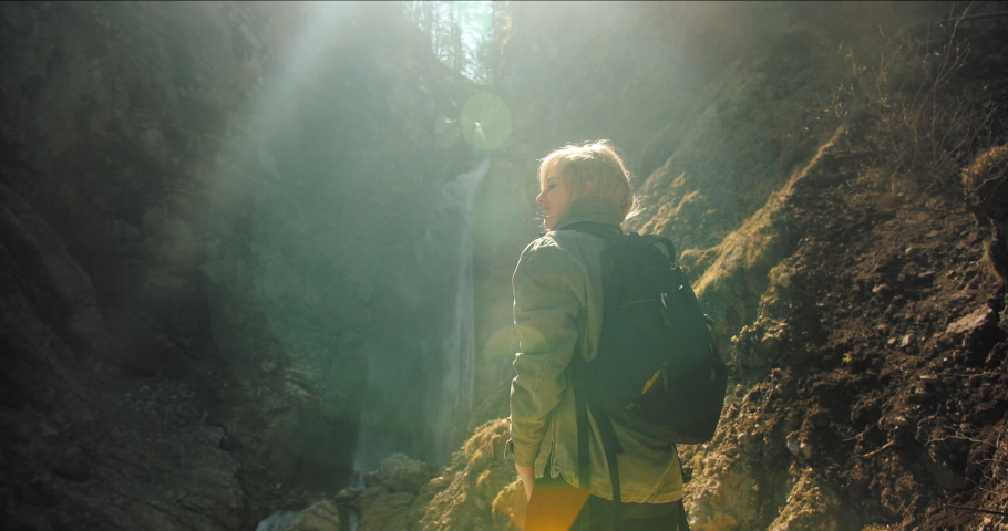 A beautiful young girl happy to hike to a waterfall with hands in the air in slow motion