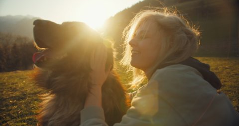 A happy girl smiling while cuddling her big fluffy beautiful dog in the sunset in slow motion