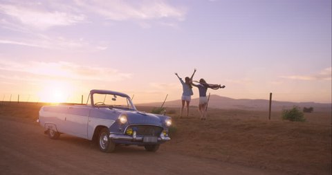 Girl friends dancing at sunset on road trip with vintage car RED DRAGON