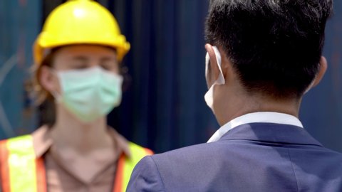factory worker in mask face and using measures temperature check body temperature at workplaces with a thermometer during a virus pandemic COVID-19. And man worker going pass inside factory.