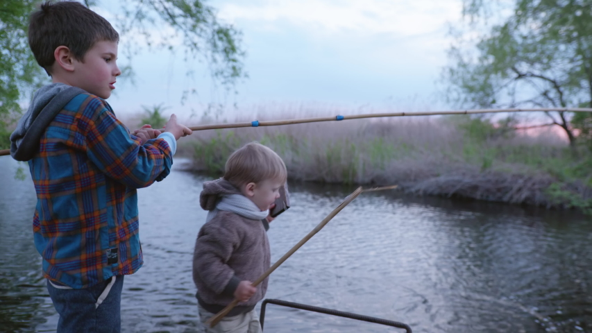 Happy weekend, little brothers with fishing rods in their hands catch fish in lake on pier among the cane on a warm evening | Shutterstock HD Video #1052841944