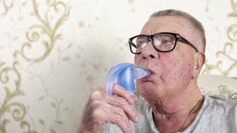 Old grandfather makes medical steam inhalations at home. Theme of a serious and incurable disease of lungs and respiratory system. Procedures for patients with COPD and other lung diseases.