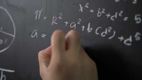 Close up teacher man hand writing math formulas on chalkboard with white chalk.