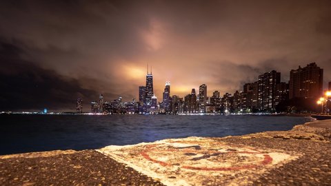 Beautiful panning up skyline cityscape timelapse of Chicago with white worn no diving sign painted on the concrete pavement in foreground and heavy cloud cover lit up from building and city lights.