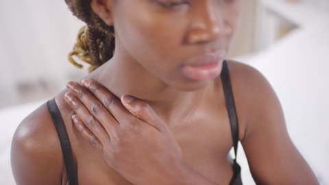 Multiple footages of cheerful black woman in lingerie applying moisturizing cream to her skin and smiling