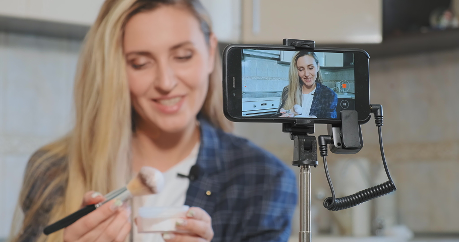 Young woman raises and shakes makeup brush producing powder cloud smiling cheerfully at smartphone on tripod slow motion closeup | Shutterstock HD Video #1052850329