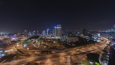 Aerial time lapse of Johor Bahru city with tall buildings in clear sky at night and busy traffic on elevated highway leading to CIQ. Prores 4KUHD