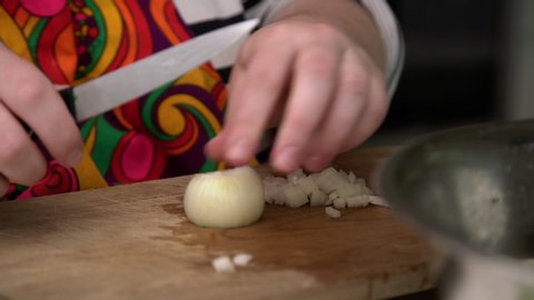 Chef cuts her self with a knife while slicing onion on wooden cutting board in the kitchen.
