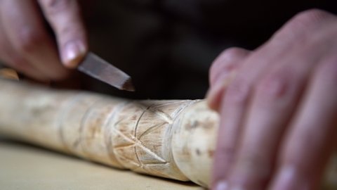 Close up process of man making wooden walking stick indoors during quarantine. Carving wood stick on the table using knife

