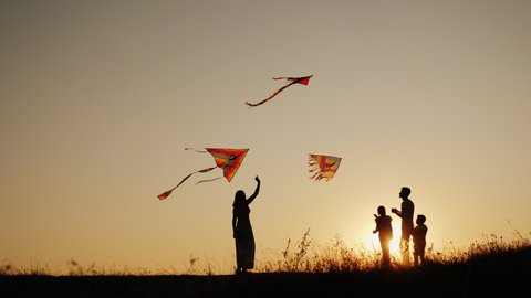 A young sam with two children plays kites at sunset in a picturesque place. Family activity outdoors