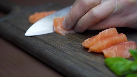 Sushi Chef Slices fresh Salmon on the sushi bar. Chef cutting salmon fillet at professional kitchen. Closeup chef hands slicing fresh fish slice in slow motion. Professional man cutting red fish