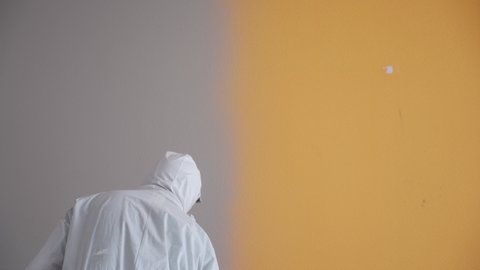 Professional painter paints the walls with white paint spray gun.