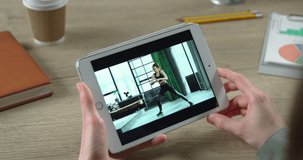 Close up of tablet screen with video of female athlete doing workout in room. Woman watching online video on device with beautiful Caucasian female fitness trainer who is doing side lunges.