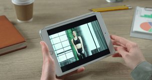 Girl watching home workout in online video chat in room. Woman having video conference on device with beautiful Caucasian female fitness trainer who is doing exercises indoor. Close up tablet screen