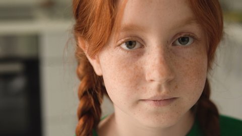 Shy red haired girl 7 years old looking at camera, shaming. School kid portrait