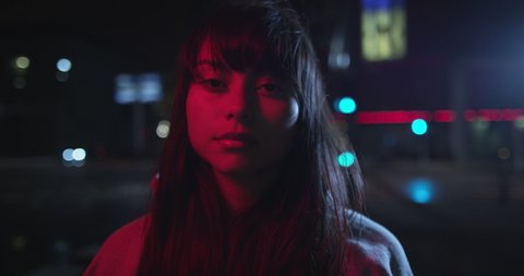 Young trendy ambitious woman looking intense in the camera at night next to neon light. Nightlife youth and urban atmosphere of girl looking to camera. Shot on RED.