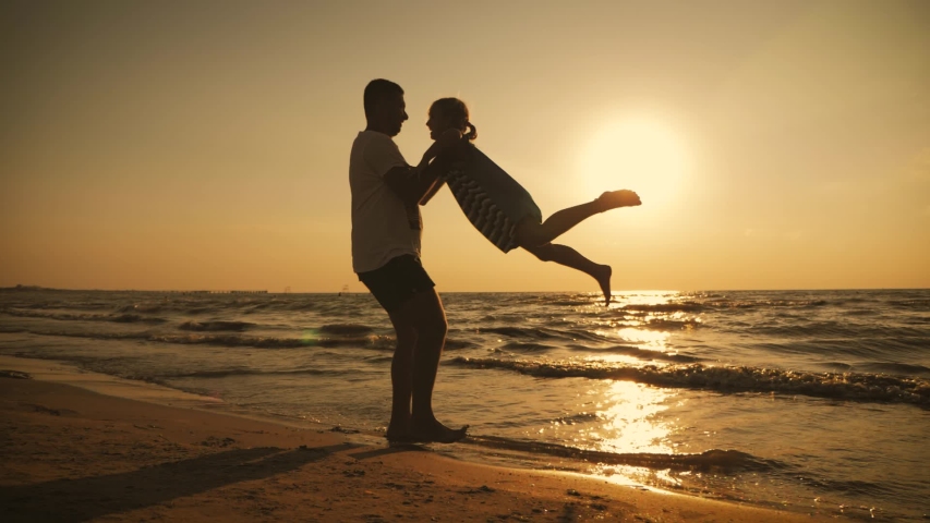 Silhouettes father and daughter play on the beach at sunset. Concept of friendly family, travel, lifestyle. | Shutterstock HD Video #1052859041