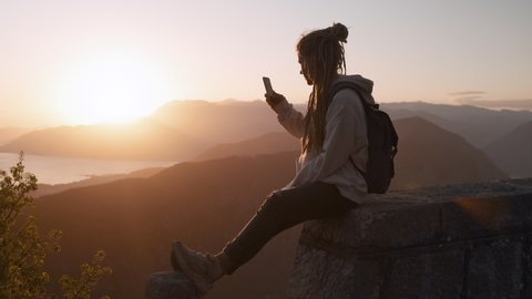 Hipster millennial Dreadlocks woman taking photo on smart phone with mountain at sunrise in slow motion, watching the sunset with beautiful landscape in Montenegro.
: film stockowy
