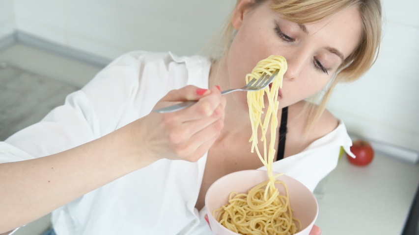 Young woman enjoying long Italian spaghetti on kitchen, quick not healthy snack
