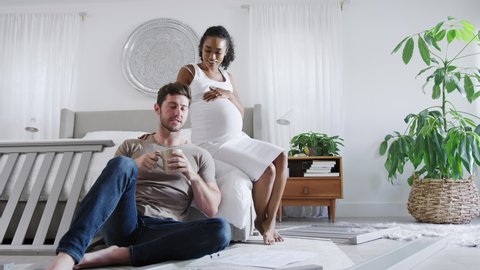 Interracial couple with pregnant woman in bedroom looking at instructions for self assembly baby cot - shot in slow motion