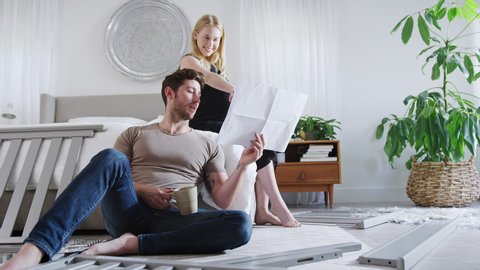 Young couple with pregnant woman in bedroom looking at instructions for self assembly baby cot - shot in slow motion