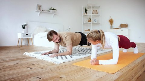 Young couple is doing plank plank exercise at home in cozy bright bedroom, slow motion. Stay at home concept