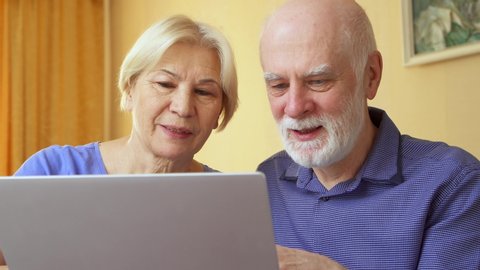 Senior couple at home using laptop. Retired family working on computer learning social media. Computer literacy among elderly people, active modern lifestyle on retirement
