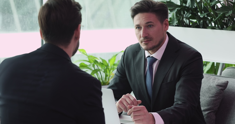 40s focused confident human resources manager in formal wear holding job interview with skilled young male candidate. Two businessman discussing project ideas at negotiations meeting in modern office. Royalty-Free Stock Footage #1052867000