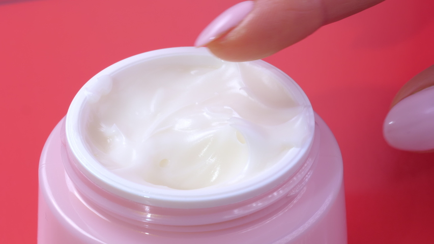 A woman takes a white hand cream from a pink jar with her finger. The concept of beauty and health and skin care for the body, face and legs. Macro. Close up view on a red background | Shutterstock HD Video #1052875142