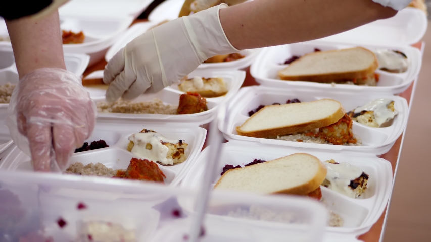 close-up, Volunteers pack free hot meals in lunchboxes, to be delivered to poor people during covid19 lock down. food delivery. Charity project, donating aid, Royalty-Free Stock Footage #1052876222