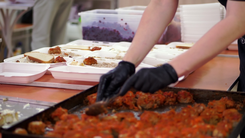 close-up, Volunteers pack free hot meals in lunchboxes, to be delivered to poor and homeless people during lock down of covid19. food delivery. Charity project, donating aid, Royalty-Free Stock Footage #1052876249